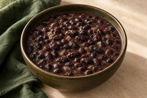 Black beans in dark broth with softened onion, in a ceramic bowl; AI illustration.